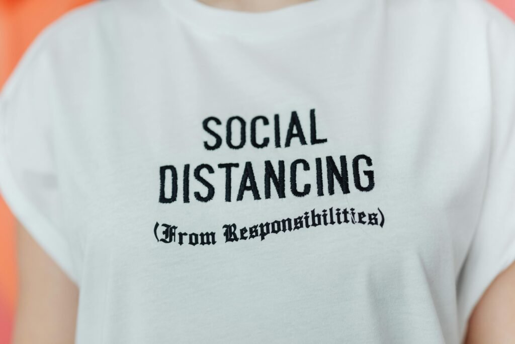 Close-up of a white T-shirt with 'Social Distancing' embroidered in black text.